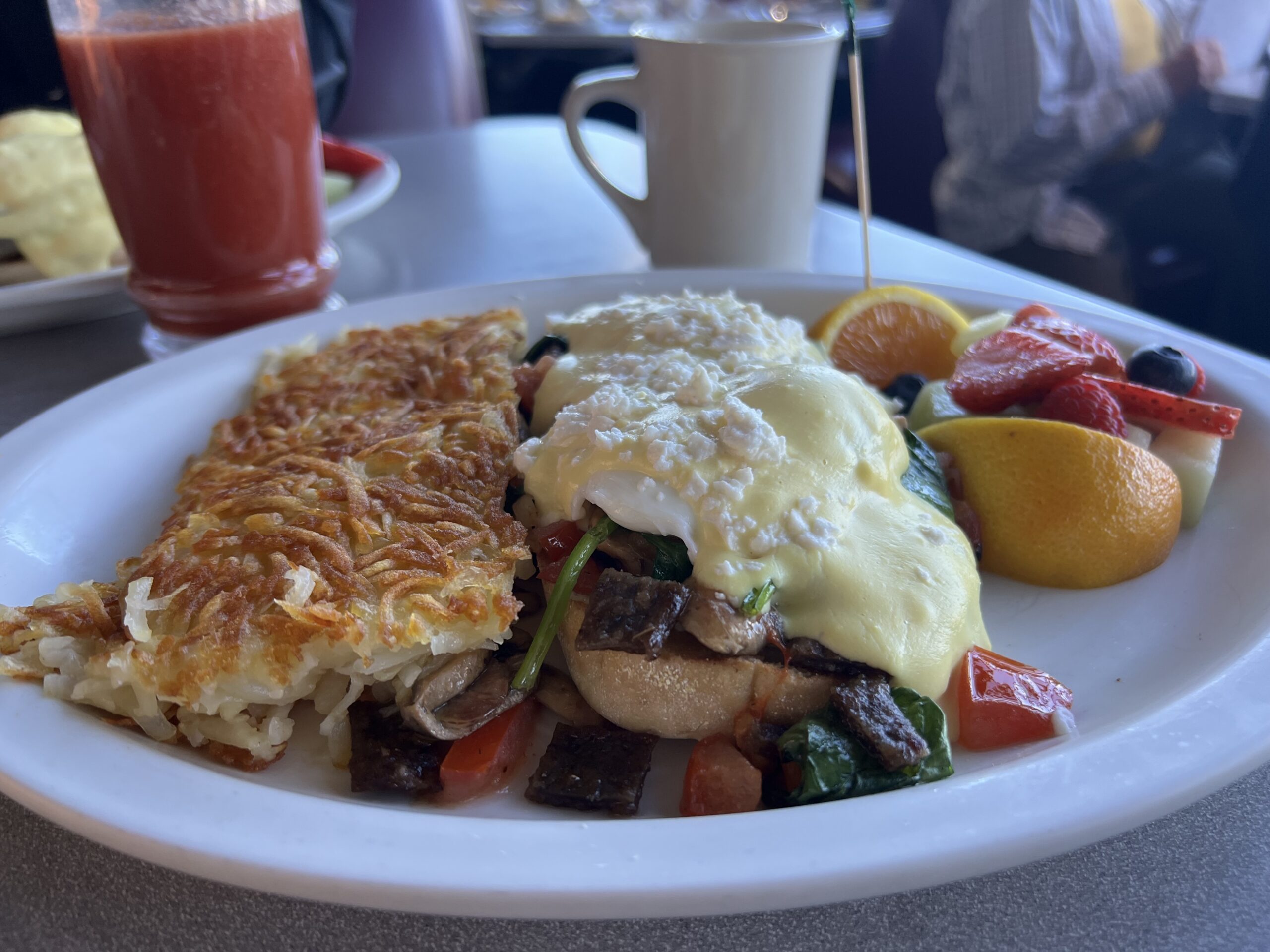 A Greek Benedict with poached eggs, fresh spinach, onion, green pepper, mushrooms, feta cheese, tomatoes, gyro meat on a toasted English muffin.