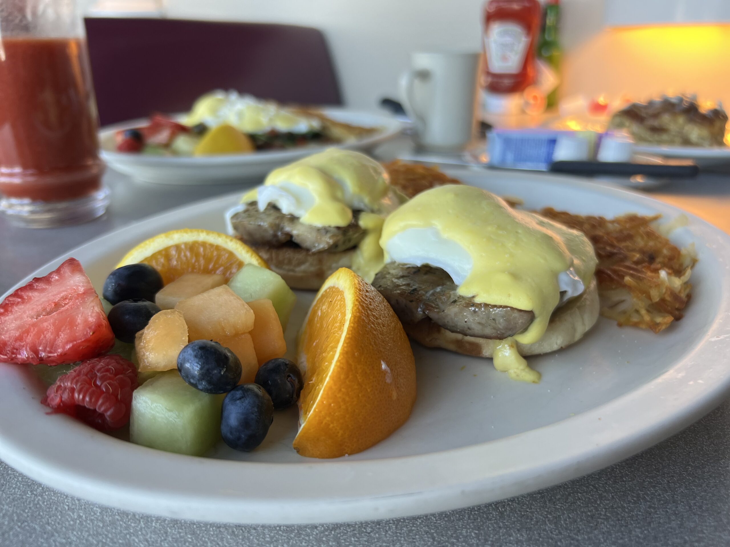 A plate of Sausage Benedict featuring poached eggs, sausage patties, and hollandaise sauce on an English muffin.