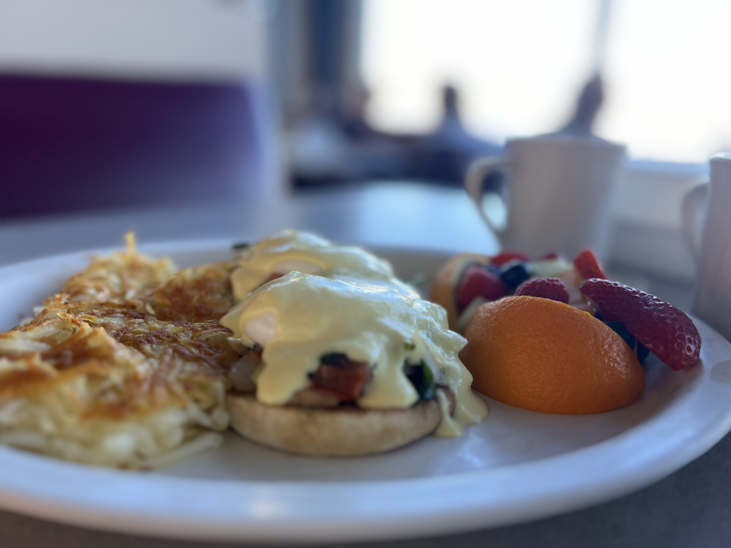 A Vegetarian Benedict with poached eggs, fresh spinach, onion, tomatoes, green peppers, and mushrooms on a toasted English muffin, topped with hollandaise sauce.